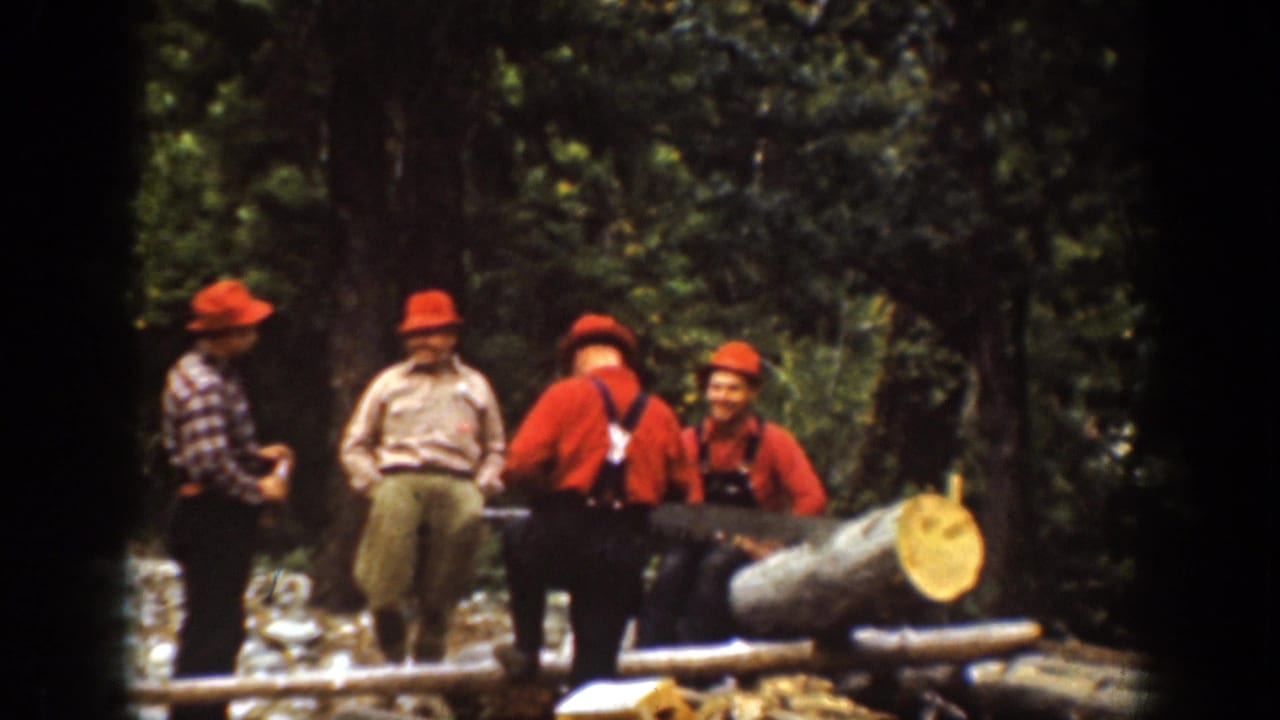 In the Chelan 1939 home-movie frame, men in red caps gather around a long felled log among tall trees.