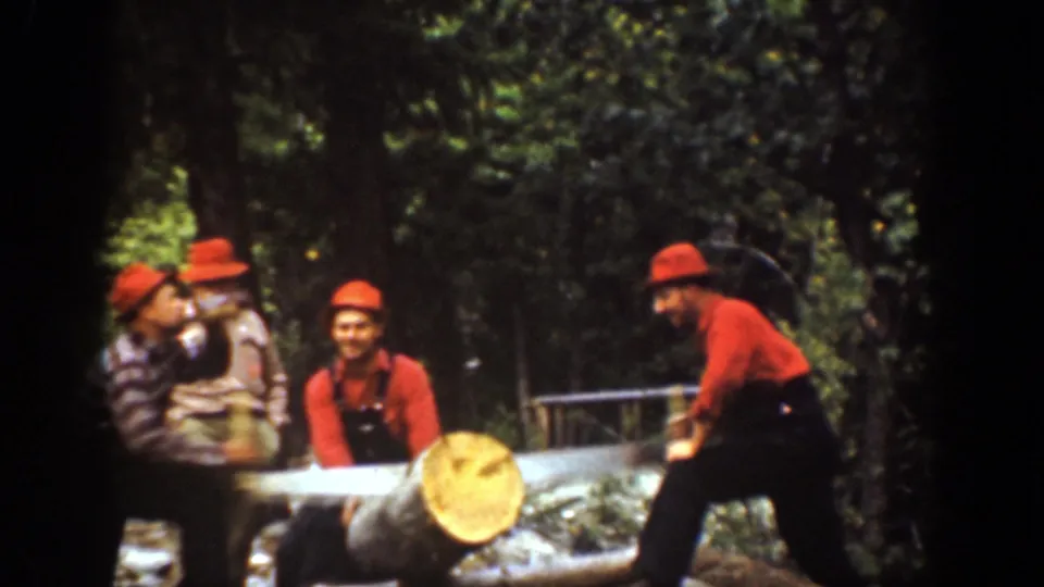 Chelan, Washington 1939 home-movie frame of men in red hats gathered by a large log as one worker handles the saw setup.
