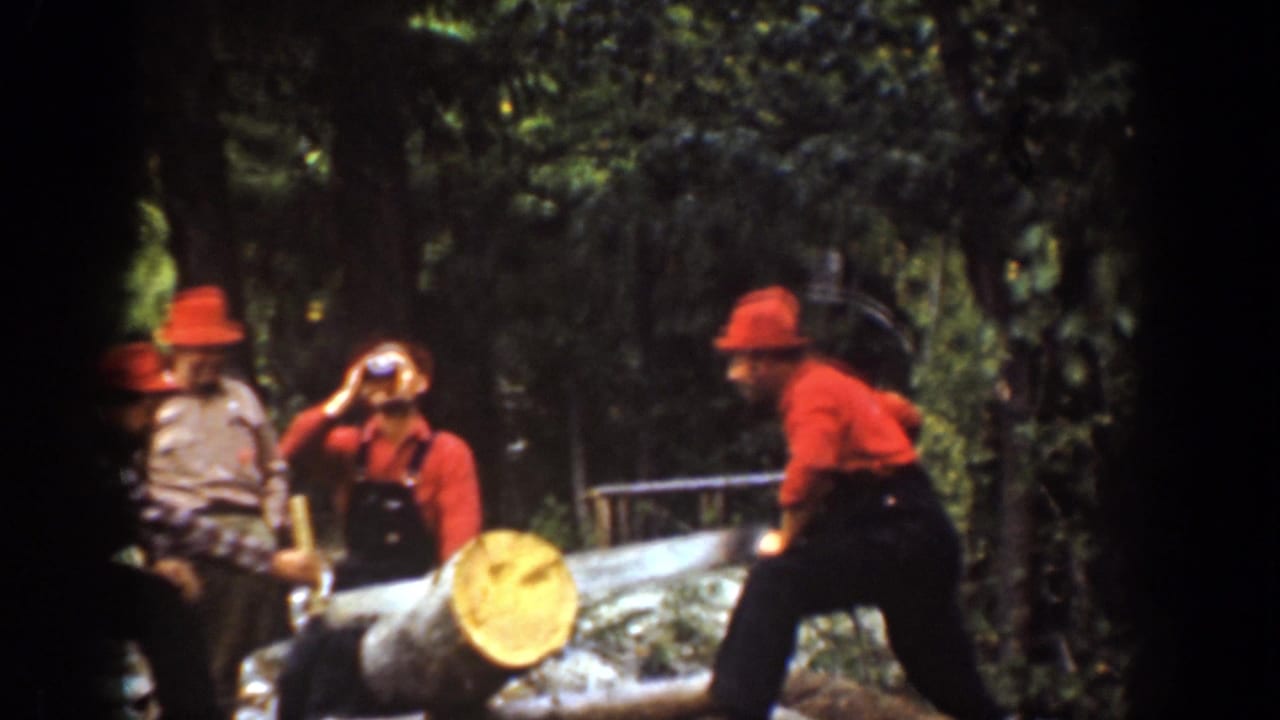 Chelan, Washington 1939 home-movie frame of logging men pausing by a log, with one man drinking and another bent toward the work.