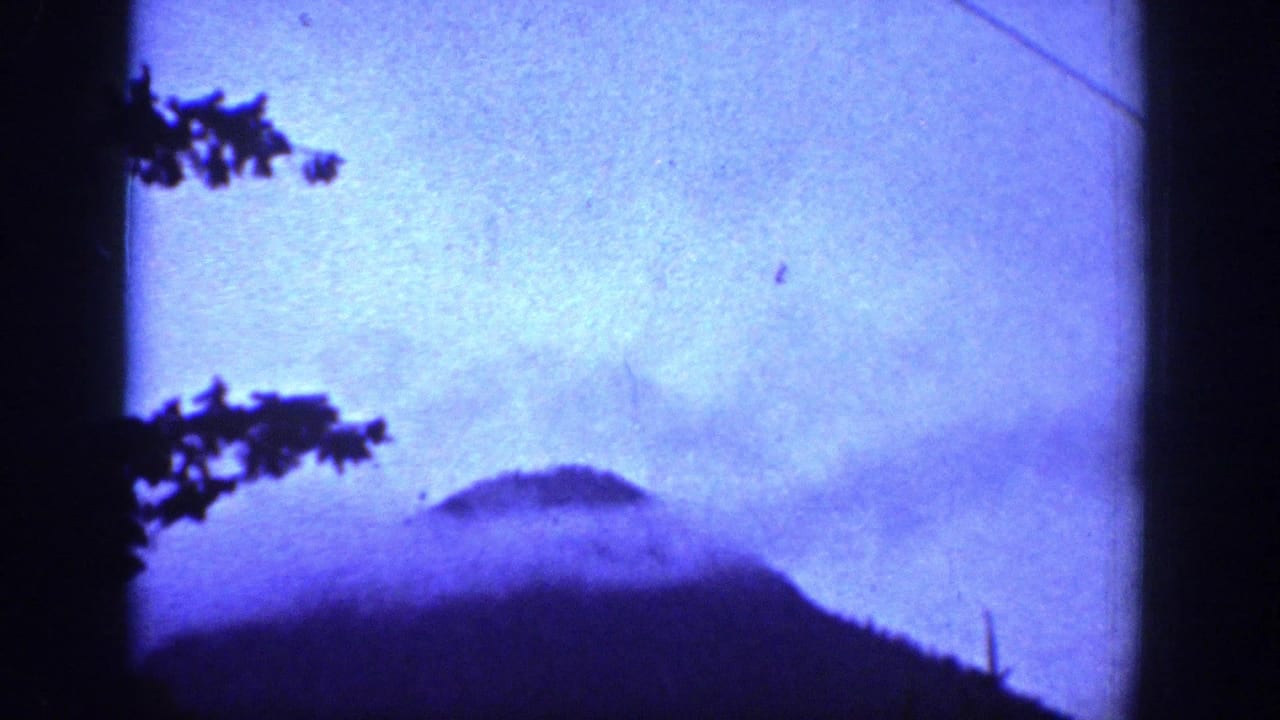 Blue-tinted 8mm view of misty mountain shapes near Chelan, Washington, with dark tree silhouettes along the frame edge.