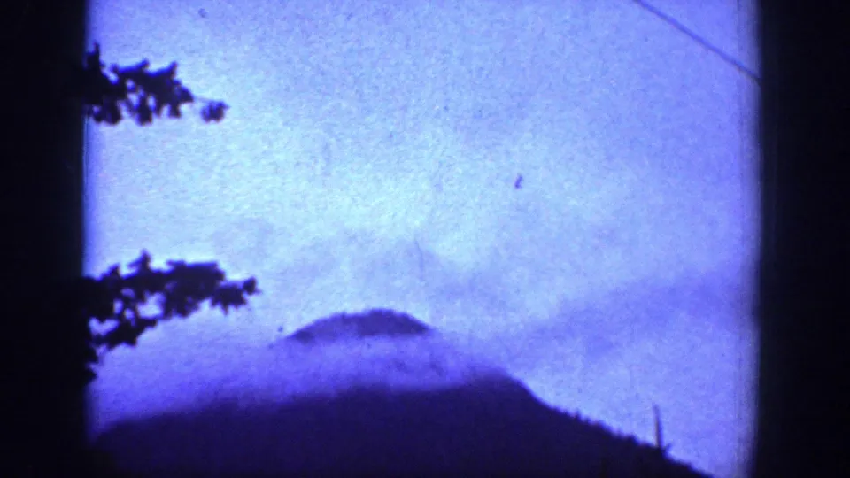 Blue-tinted 8mm view of misty mountain shapes near Chelan, Washington, with dark tree silhouettes along the frame edge.