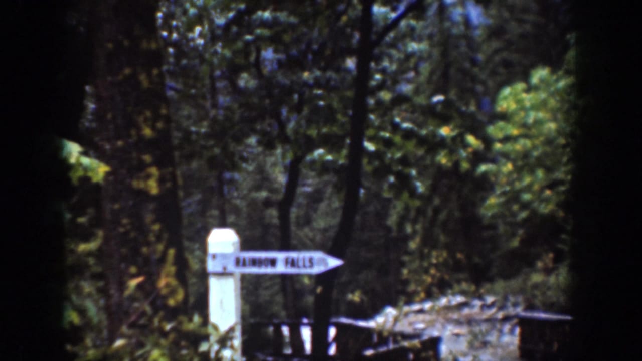1939 Chelan, Washington frame showing a white arrow sign marked Rainbow Falls along a shaded forest trail.