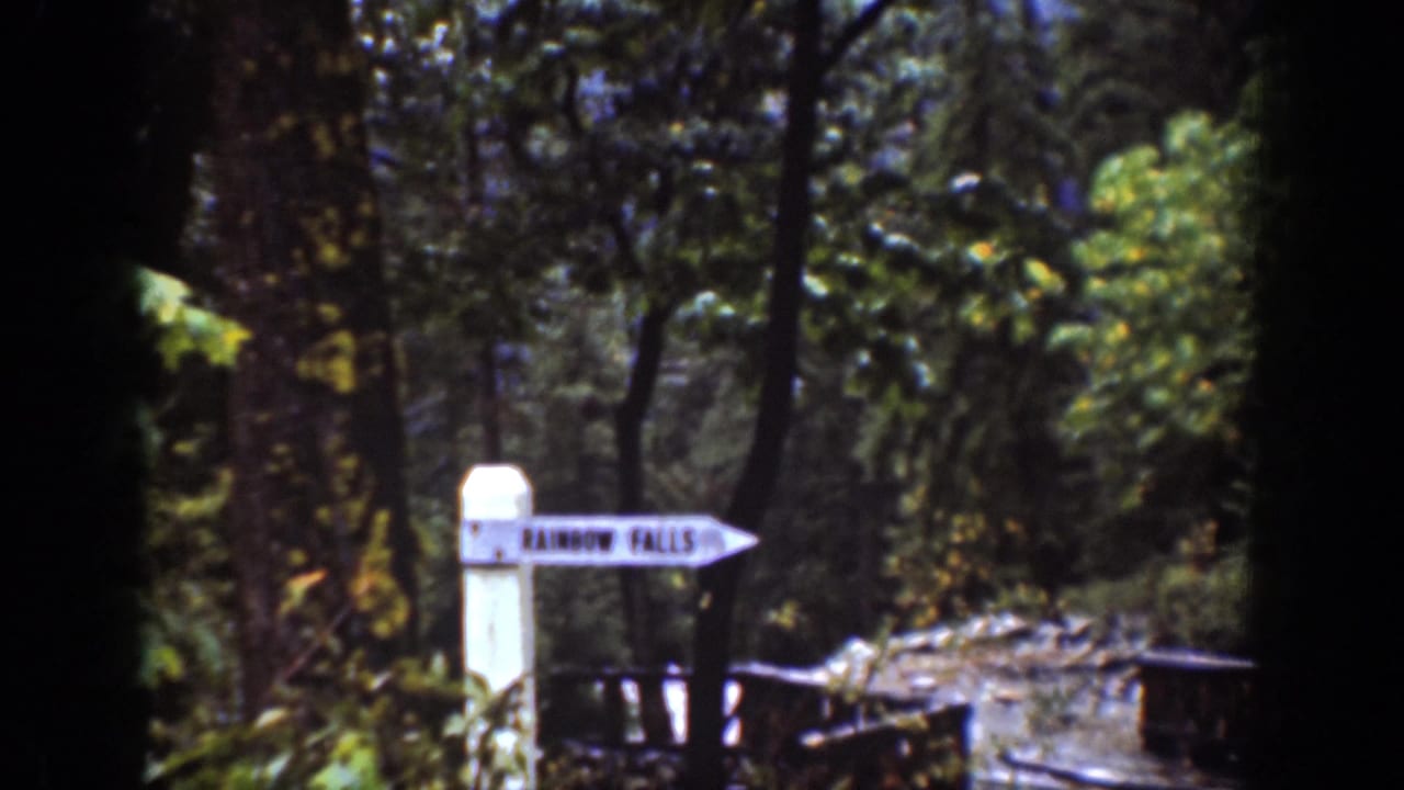 White signpost reading Rainbow Falls beside a forest path.