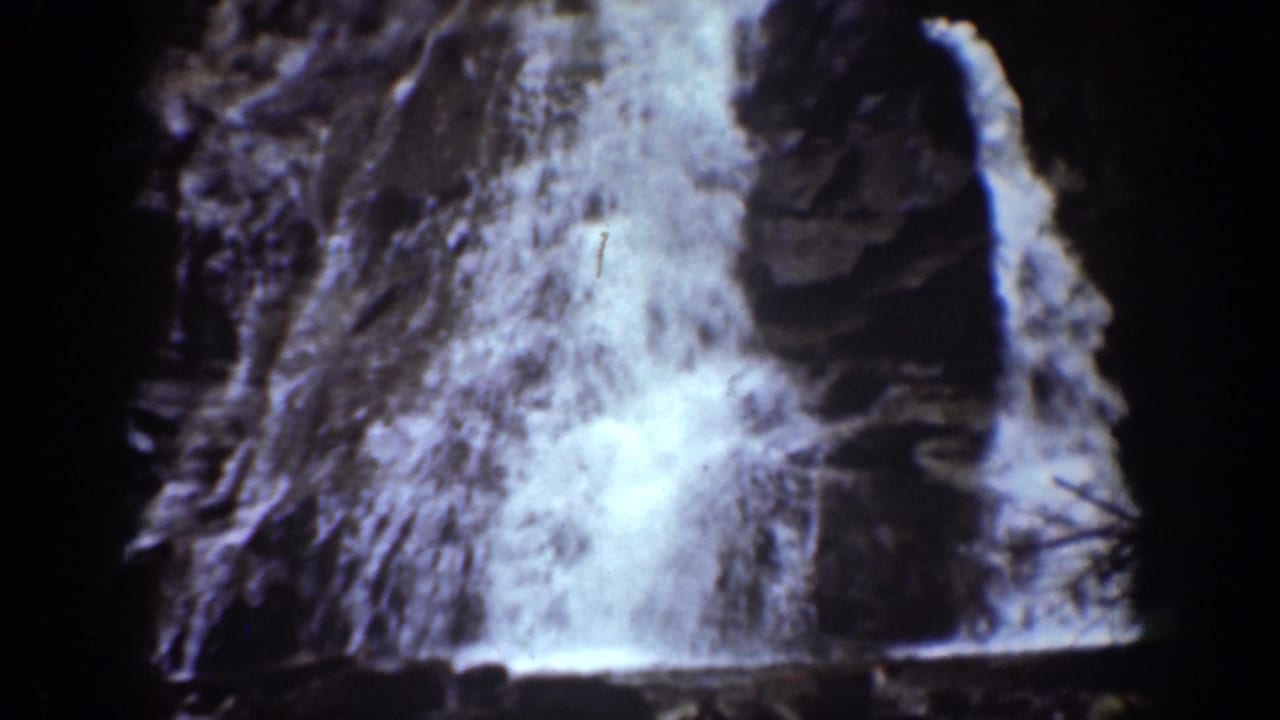Close view of water falling over dark rocks in a shadowed ravine.