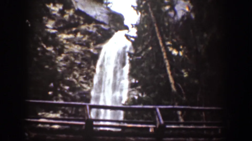 1939 Chelan, Washington home-movie frame showing a waterfall behind a narrow bridge in a dark rocky forest setting.