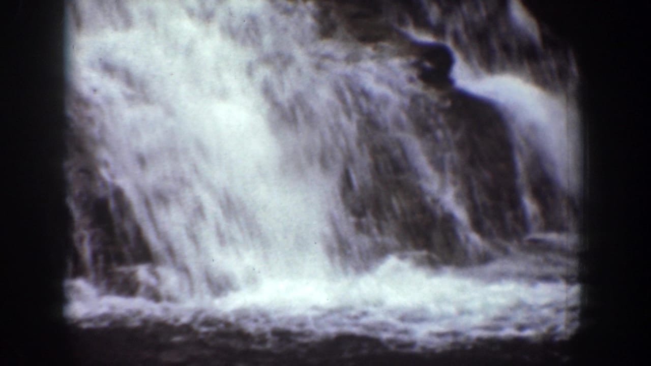 Close 8mm view of frothy waterfall water rushing over dark rock, from the Chelan, Washington home-movie clip.