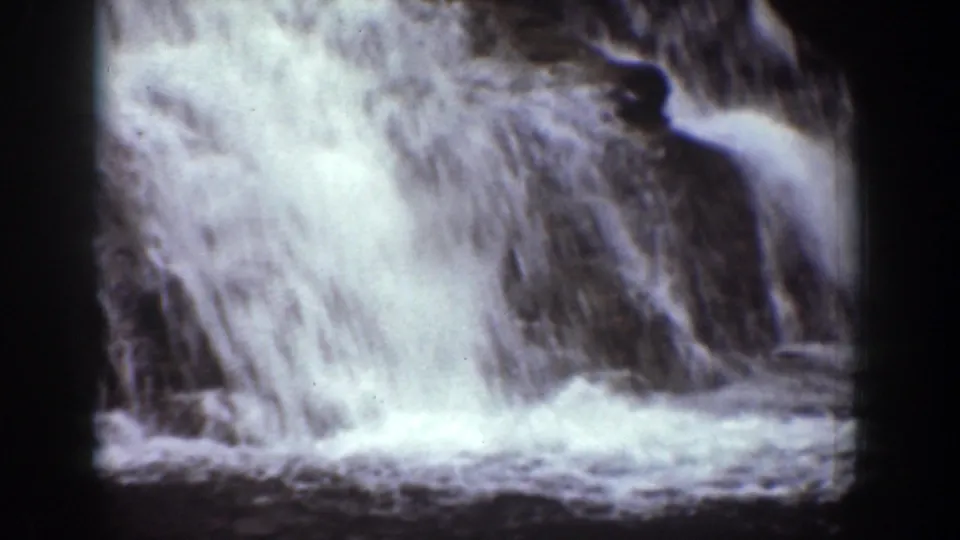 Close 8mm view of frothy waterfall water rushing over dark rock, from the Chelan, Washington home-movie clip.