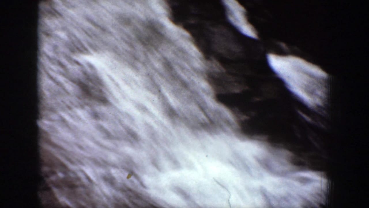 1939 8mm frame showing a diagonal sheet of white cascade water beside dark rock in Chelan, Washington.