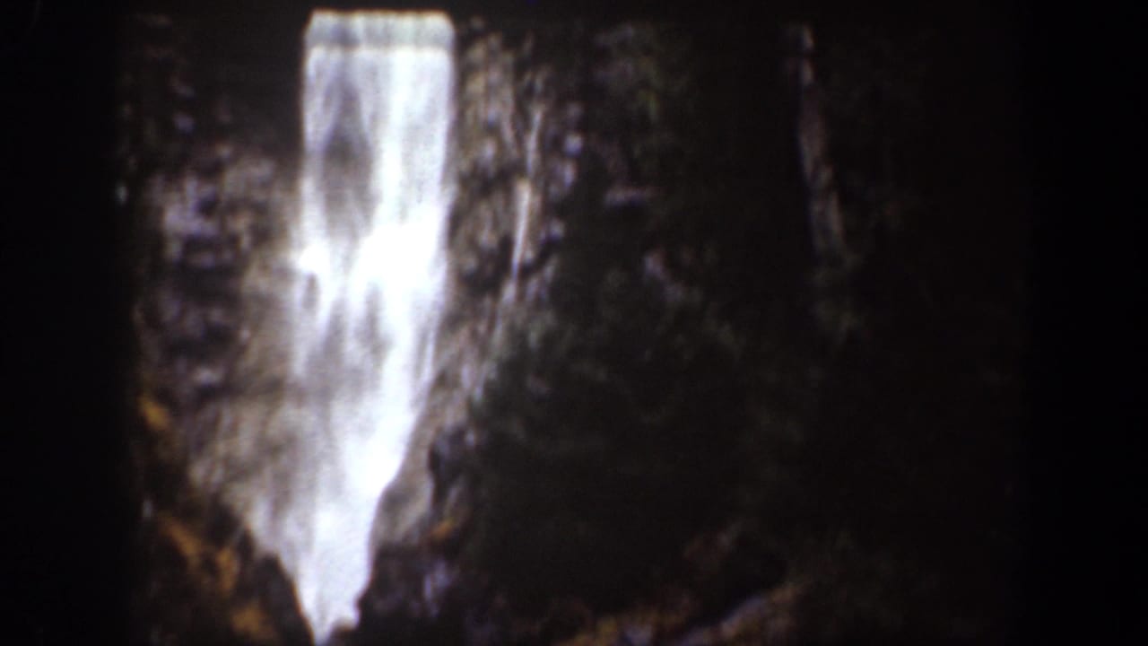 Tall waterfall descending through a dark rocky forest gorge.