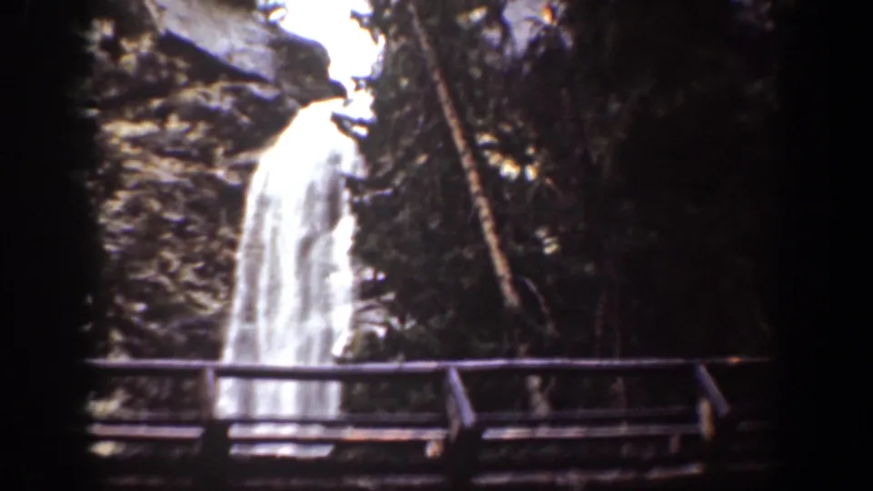 1939 Chelan, Washington view of a waterfall framed by trees, rock walls, and a wooden bridge railing.