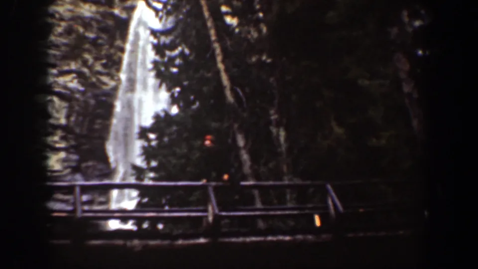 1939 Chelan, Washington home-movie frame showing a waterfall behind a wooden bridge or railing in a forested rocky setting.