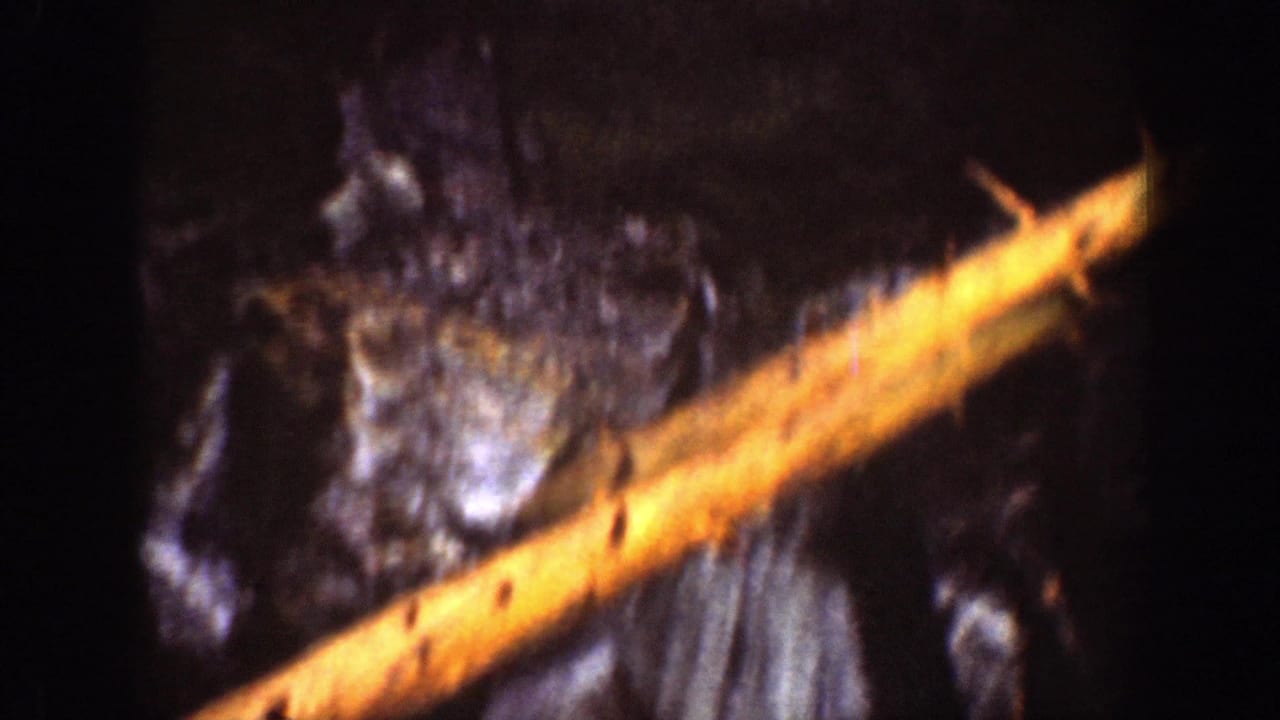 1939 8mm waterfall view with dark rocks, falling water, and a warm orange exposure streak across the frame.