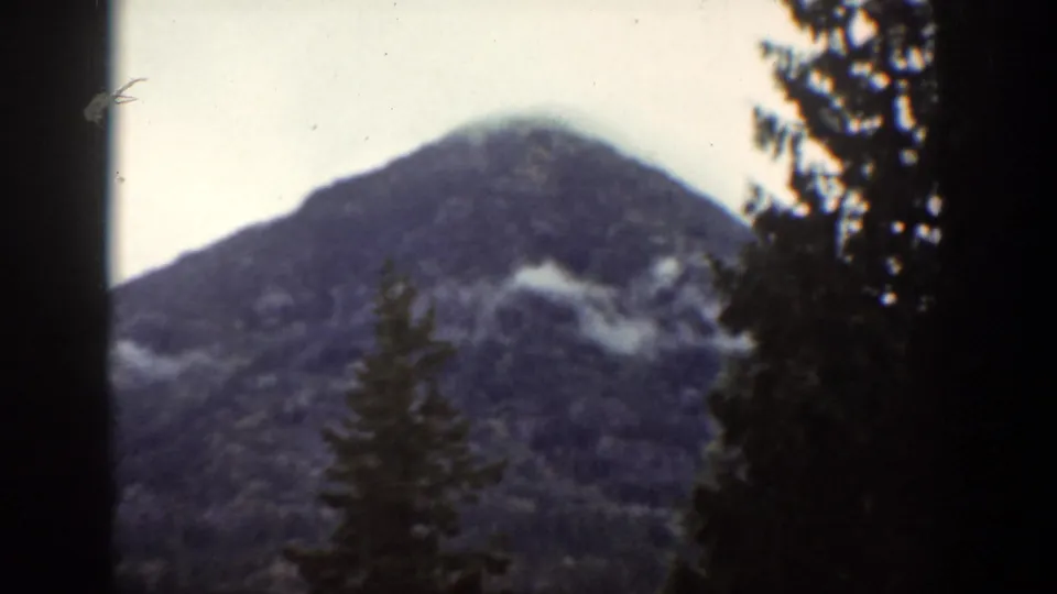 1939 Chelan, Washington home-movie view of a misty mountain peak rising behind evergreen forest and dark foreground trees.