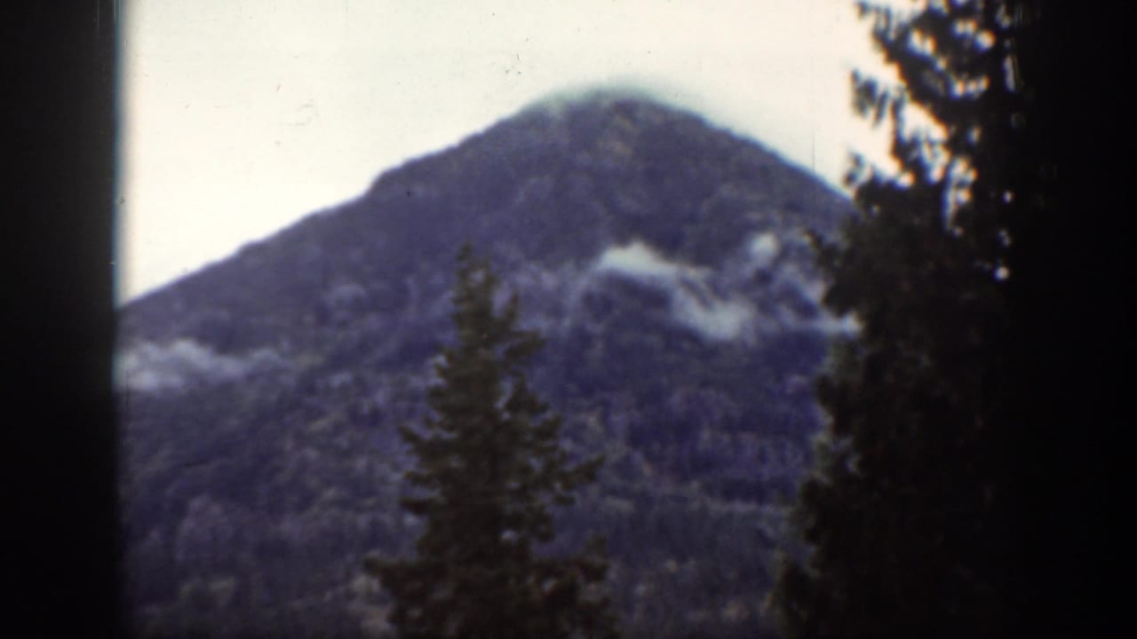Chelan, Washington mountain forest scene with evergreen trees in front of a clouded peak, seen in faded 1939 8mm color.