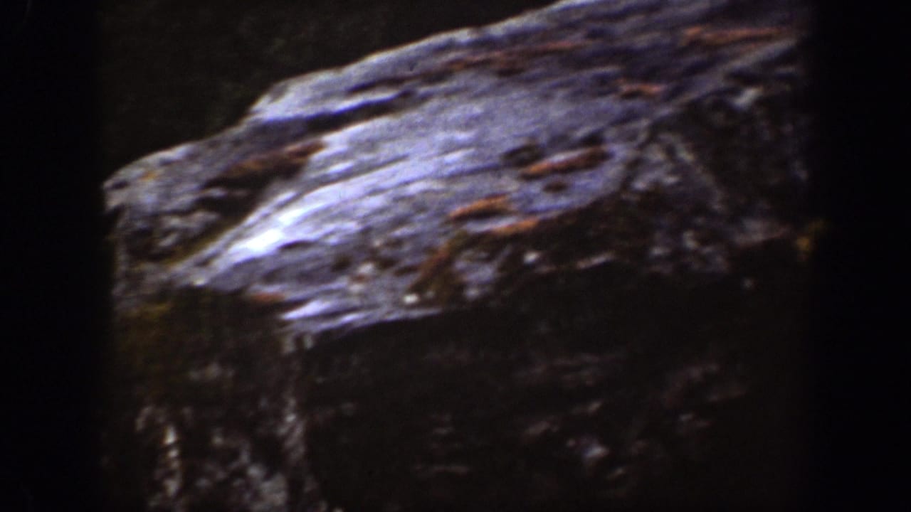 Dark interior frame with a large rough surface at left and little visible human detail.
