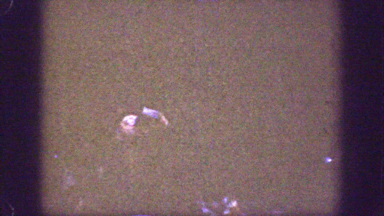 Underexposed 1939 Chelan home-movie frame with a partially visible adult figure and a small bright glass-like object in shadow.