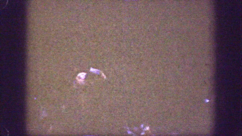 Underexposed 1939 Chelan home-movie frame with a partially visible adult figure and a small bright glass-like object in shadow.