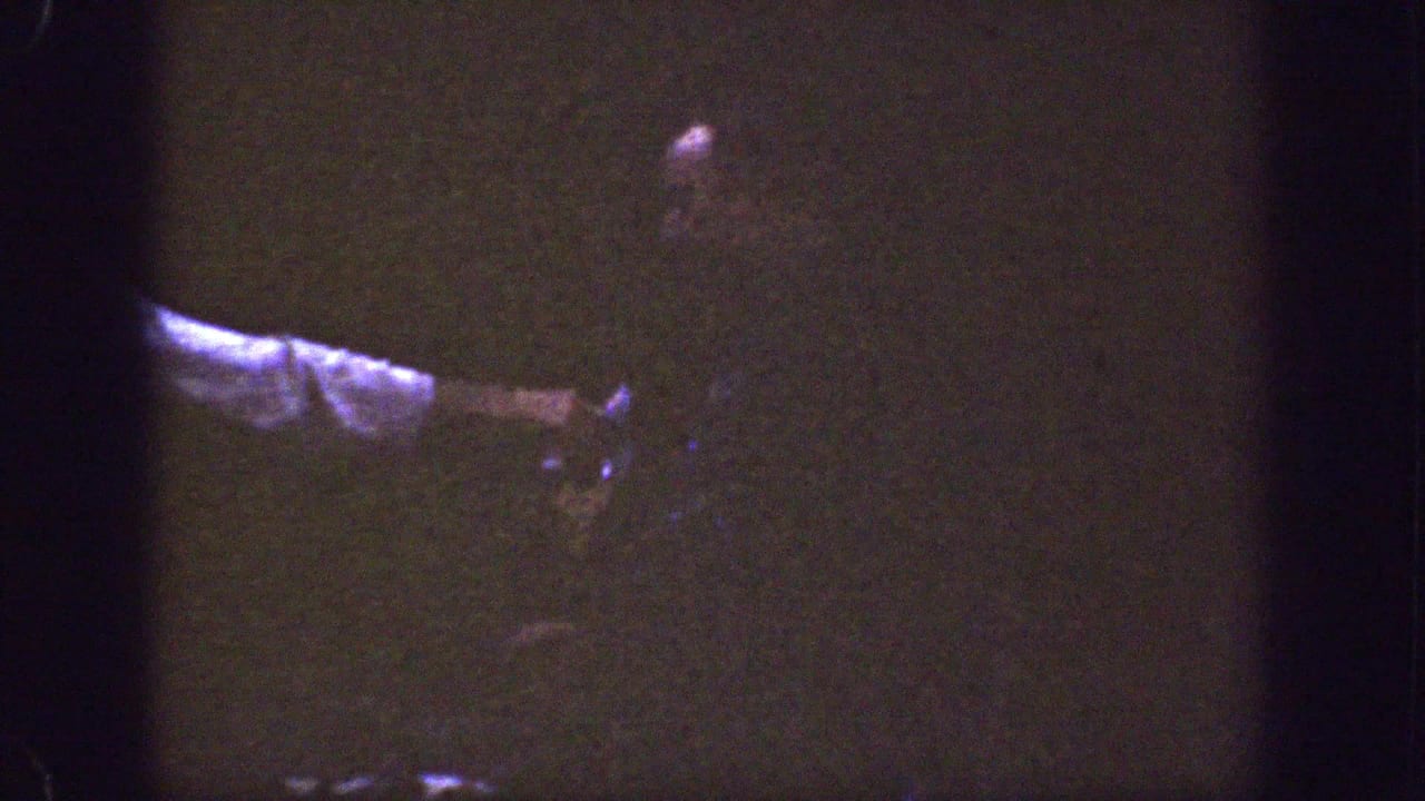 An adult figure is partly obscured in shadow, with a pale sleeve or arm crossing the lower left of the frame.