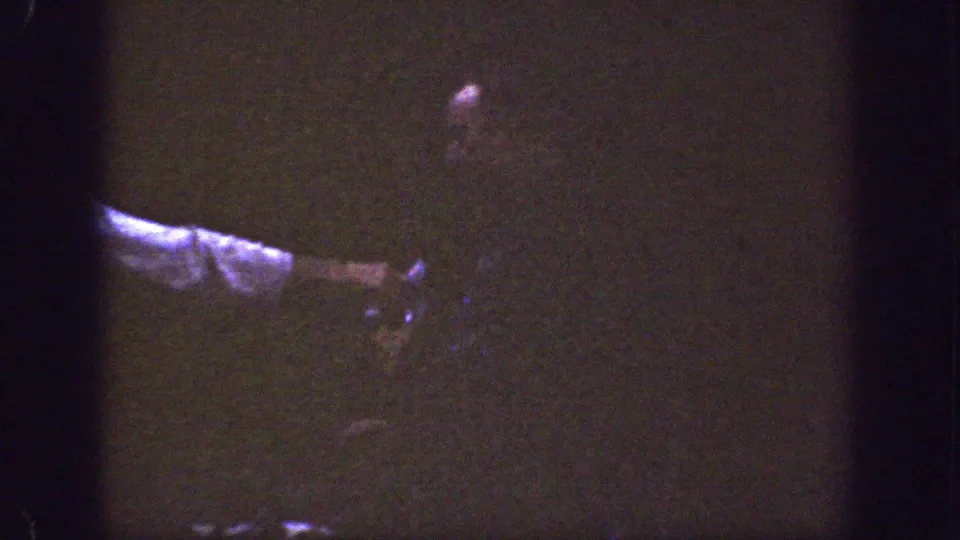 An adult figure is partly obscured in shadow, with a pale sleeve or arm crossing the lower left of the frame.