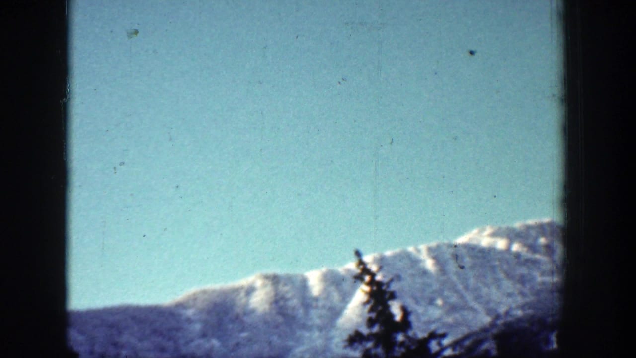 A snow-capped mountain ridge near Chelan, Washington, appears behind a dark evergreen silhouette in a 1939 8mm frame.