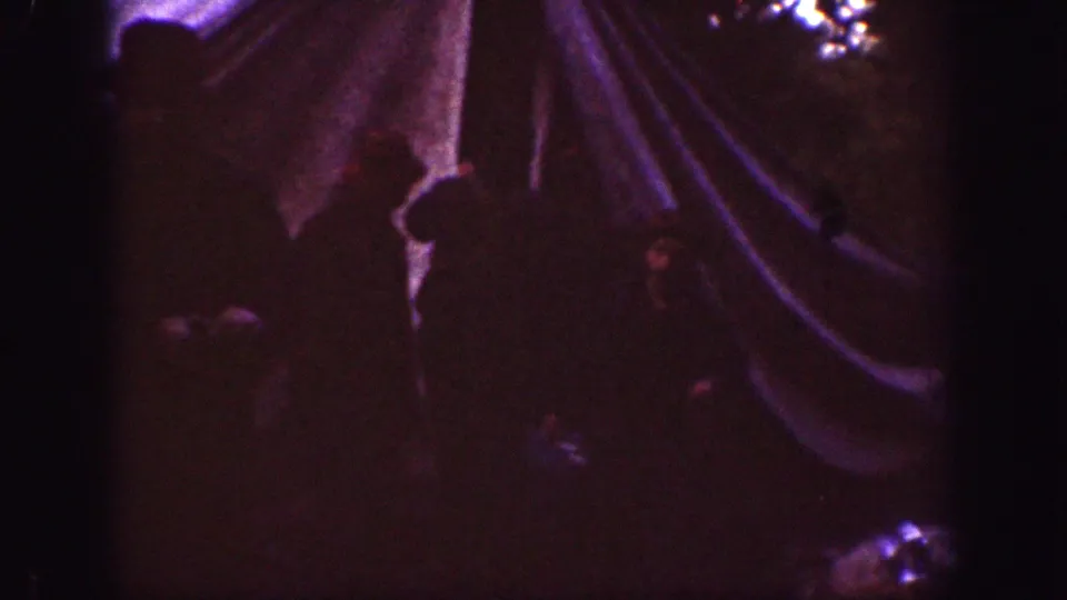 1939 Chelan campsite frame with a canvas tent or rainfly at right and a shadowed person standing nearby in low light.