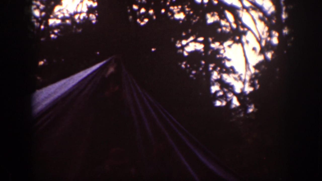 1939 Chelan campsite frame with a canvas tent shape beneath silhouetted trees and a bright patch of sky in the background.