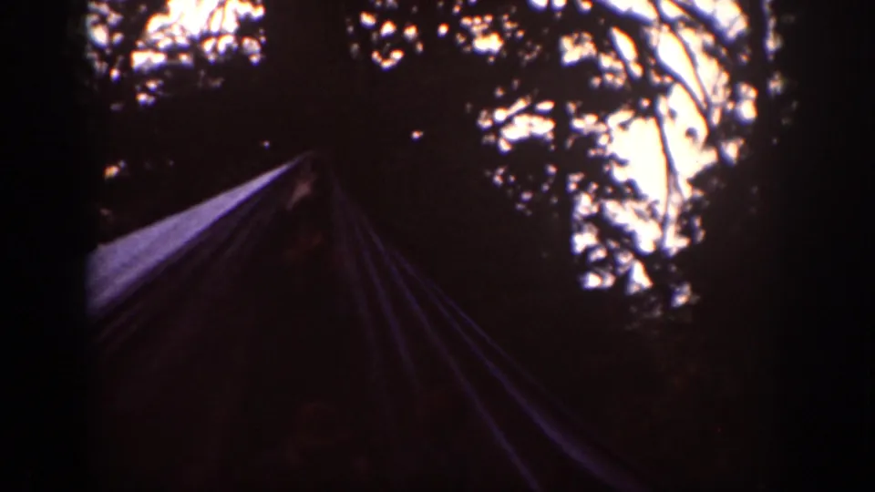 1939 Chelan campsite frame with a canvas tent shape beneath silhouetted trees and a bright patch of sky in the background.