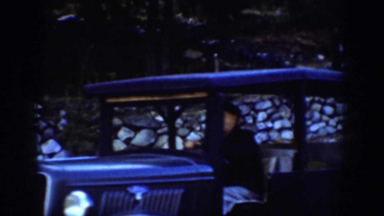 Dark open car beside a stone wall with a seated driver partly visible.