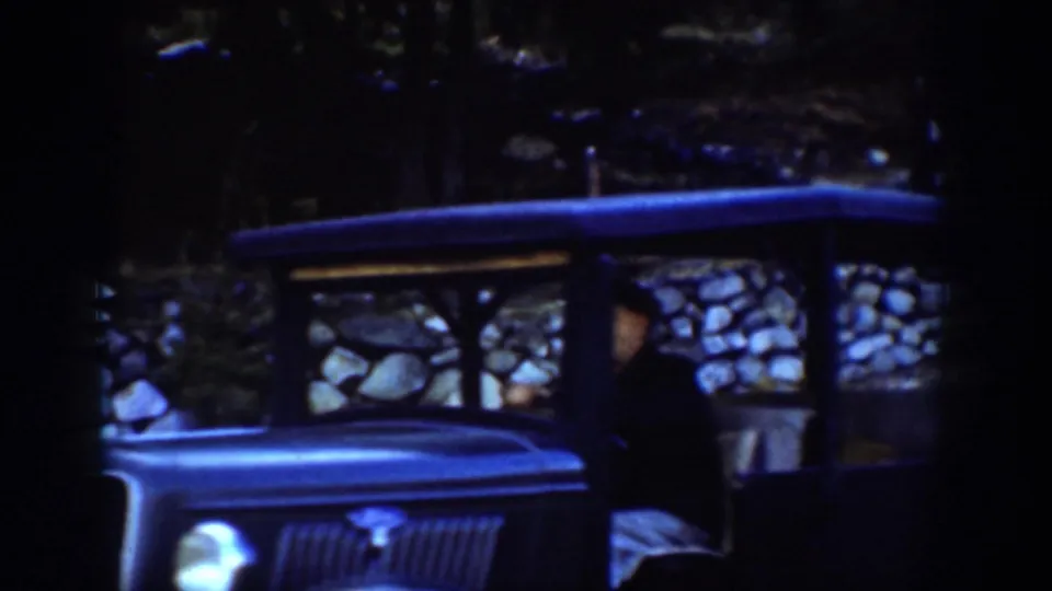 Chelan, Washington 1939 home-movie frame showing a dark open car near a stone wall with a driver in shadow.