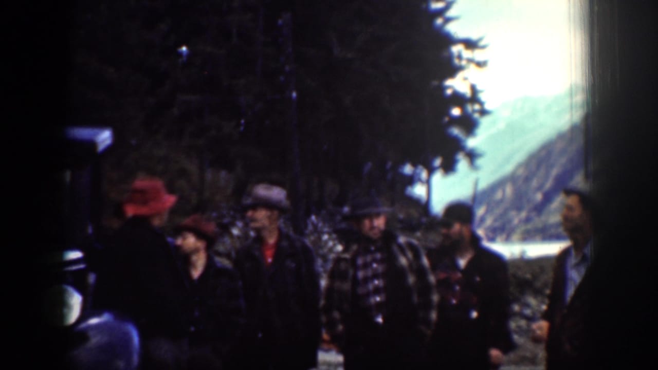 Chelan, Washington 1939 frame showing a small group in hats, including a red hat, beside a dark car with lake and mountains beyond.
