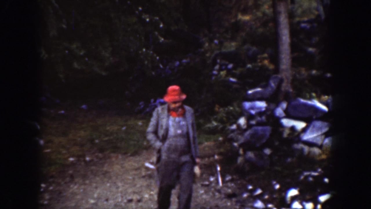 The man in a red hat and grey jacket appears closer to the camera on the wooded path in Chelan, Washington.