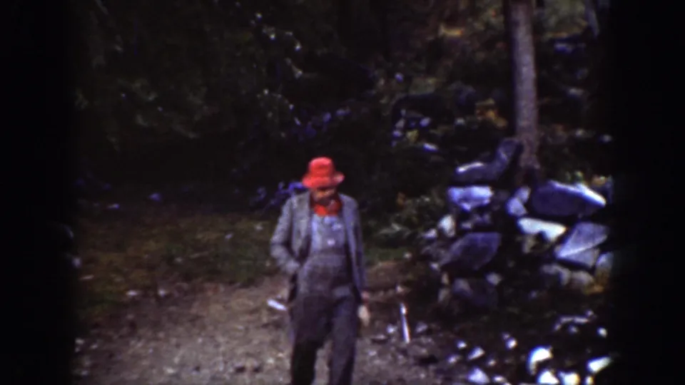 The man in a red hat and grey jacket appears closer to the camera on the wooded path in Chelan, Washington.
