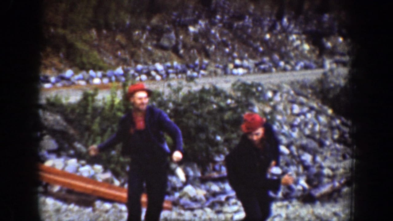 Two men in dark clothing and red caps move energetically across the rocky Chelan shoreline during a playful 1939 home-movie scene.