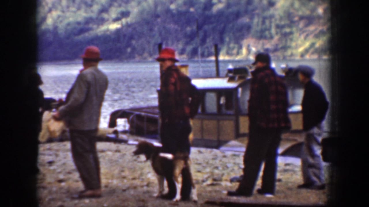 A small boat sits near the Chelan shoreline as several men and a dog stand on the rocky bank in 1939 home-movie footage.