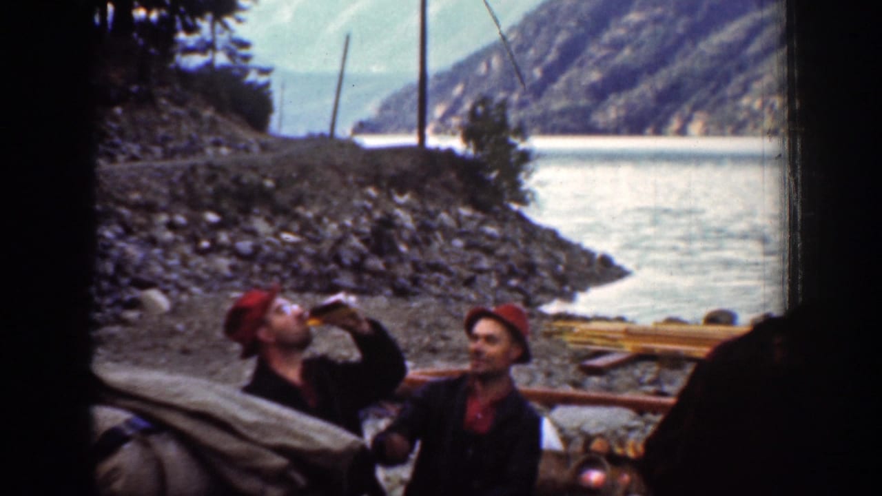 Chelan, Washington 1939 home-movie frame showing men in red hats near a rocky riverbank as one drinks from a bottle.