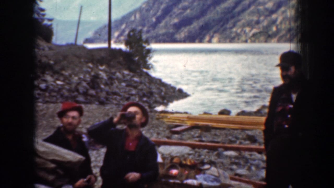 Chelan, Washington 1939 8mm frame of men on a rocky shoreline, with one drinking from a bottle and mountains across the water.