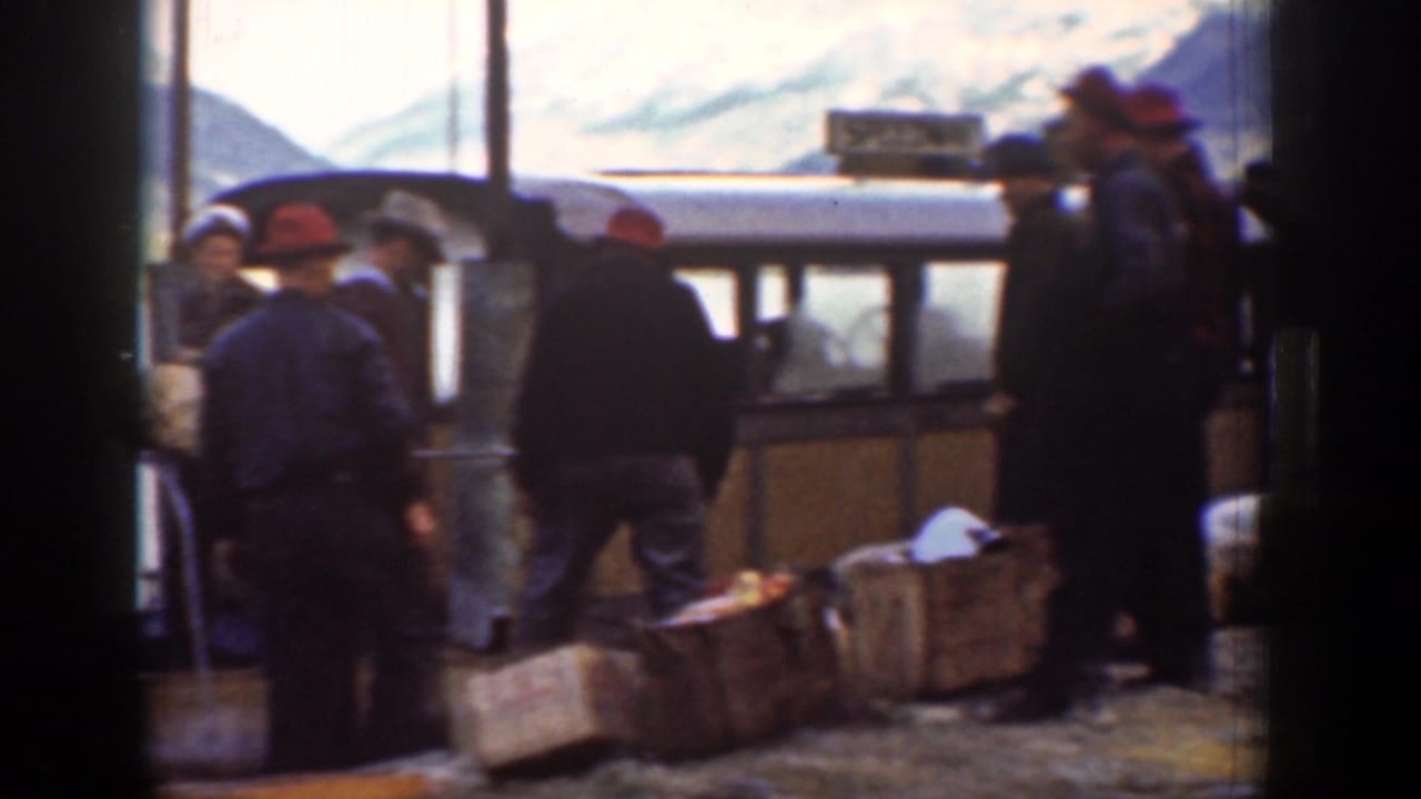 Men stand near wooden crates beside a small carriage on a gravel platform.