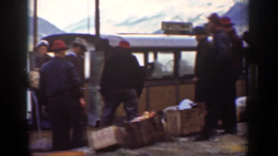 1939 Chelan, Washington home-movie frame showing men in hats near crates and parcels beside a small carriage or coach.