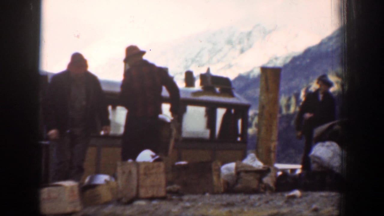 In Chelan, Washington, 1939, men in hats and work clothes stand near wooden crates beside a brown boat at a lakeside dock.