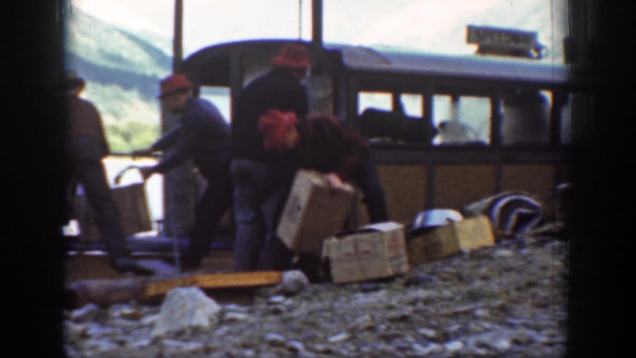 Chelan lakeside workers move wooden crates beside a brown boat, with a partially legible sign or marking above the cabin area.
