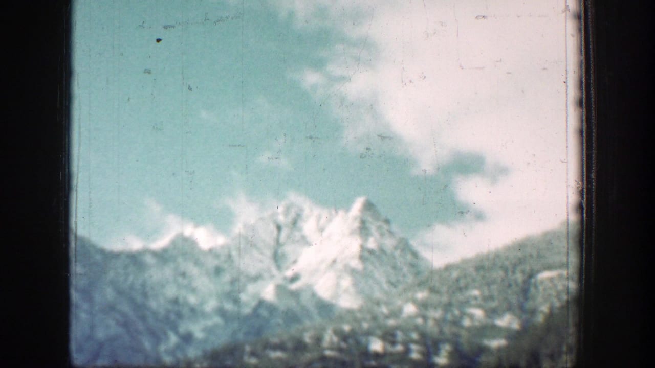 Snow-capped peaks near Chelan appear beyond green slopes in soft 1939 8mm color footage.
