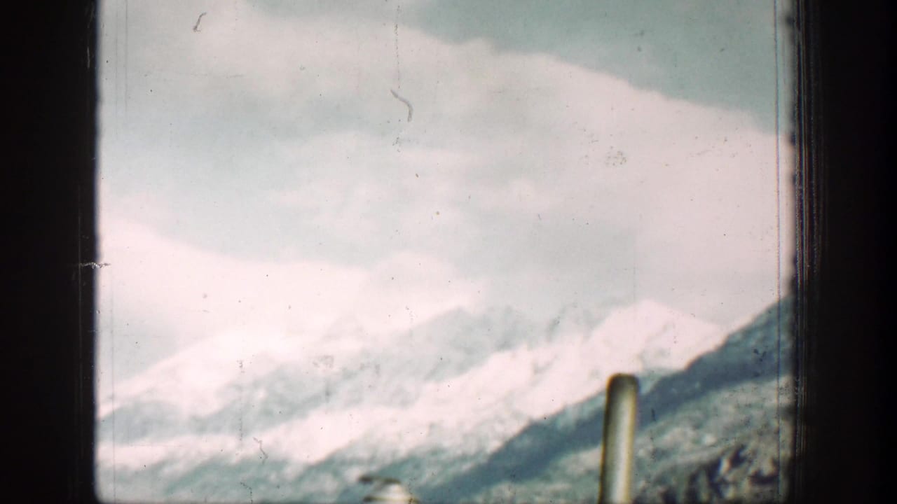 1939 Lake Chelan home-movie view of snow-capped mountains and pale lake water through a dark window frame.