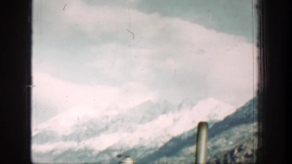 1939 Lake Chelan home-movie view of snow-capped mountains and pale lake water through a dark window frame.