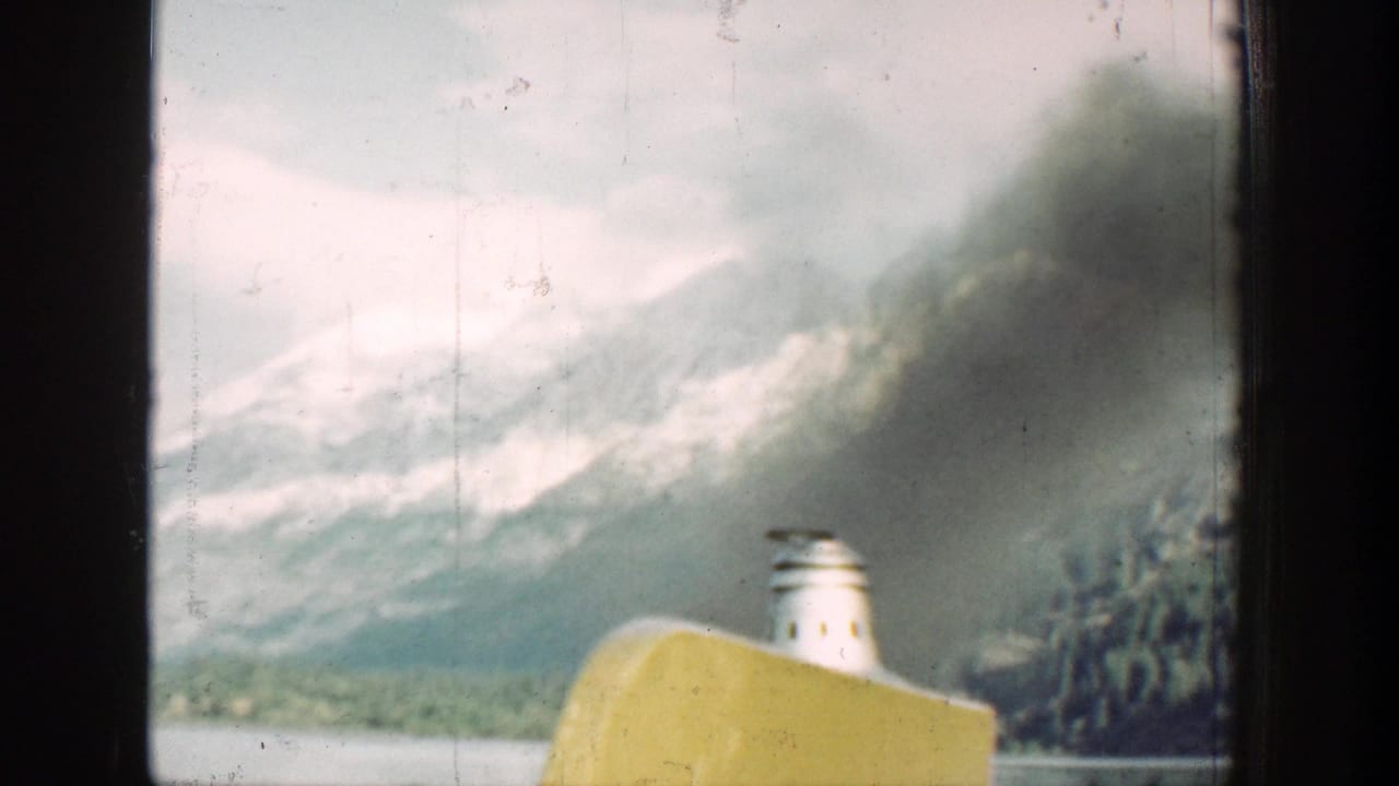 1939 Chelan boat view with a yellow hull edge, white smokestack, dark smoke, and snowy mountain backdrop.