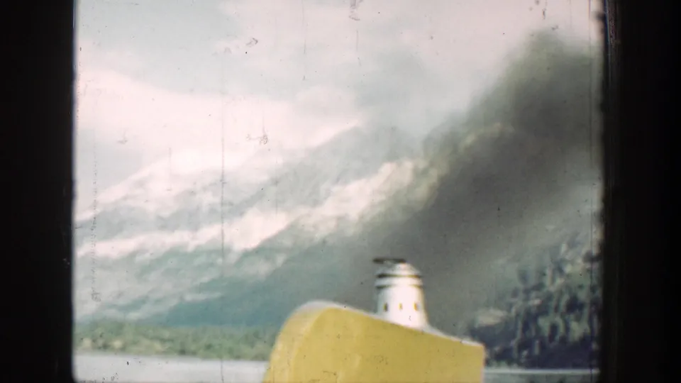 1939 Chelan boat view with a yellow hull edge, white smokestack, dark smoke, and snowy mountain backdrop.