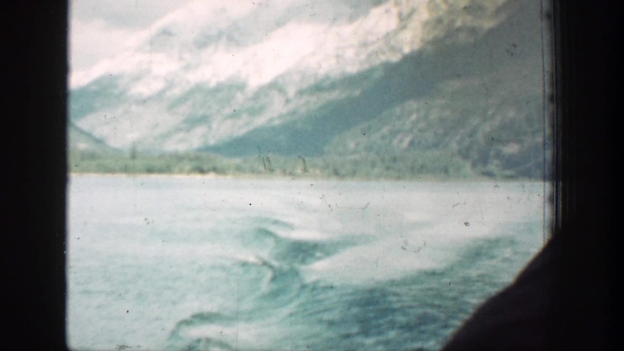 1939 Lake Chelan 8mm frame of foamy boat wake crossing the water, with mountain slopes and dark window edges visible.