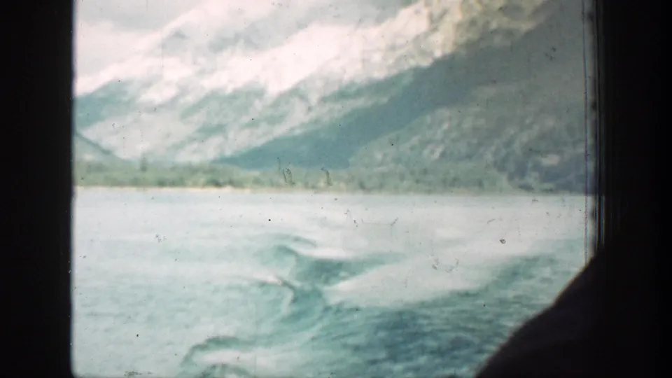 1939 Lake Chelan 8mm frame of foamy boat wake crossing the water, with mountain slopes and dark window edges visible.