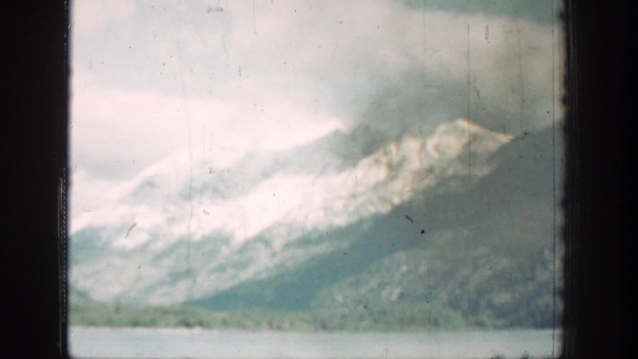 1939 Chelan, Washington home-movie frame showing a cloudy lake and distant mountain slopes through dark window framing.