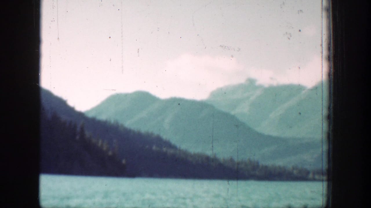 Chelan, Washington 8mm frame showing a wooded lakeside slope, turquoise water, and distant mountains under a cloudy sky.