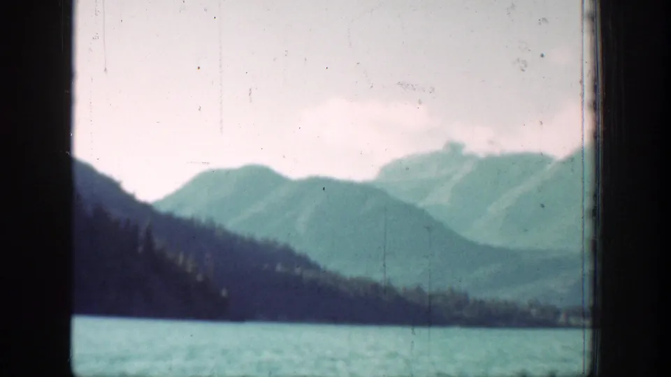Chelan, Washington 8mm frame showing a wooded lakeside slope, turquoise water, and distant mountains under a cloudy sky.